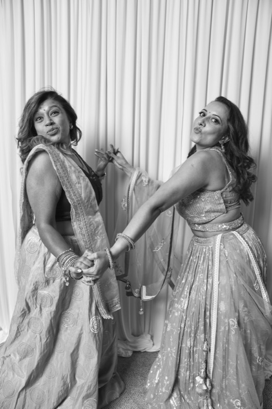 Two women in lehengas hold hands and lean apart, pouting