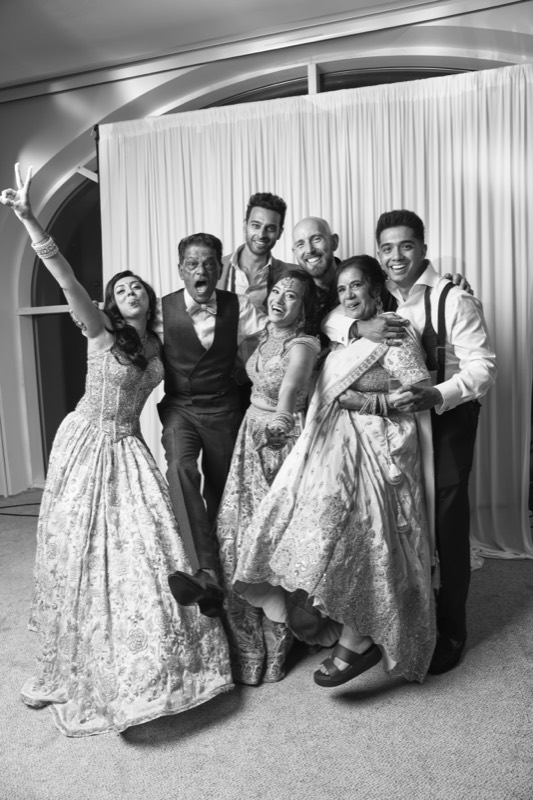 A bride with her arm flung up poses with her family and friends