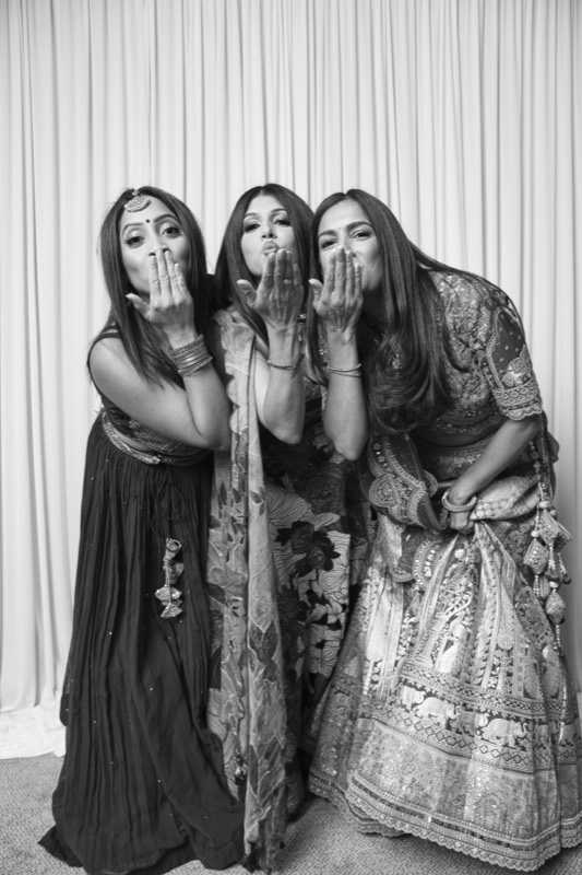 Three women in wedding outfits blow kisses at the camera